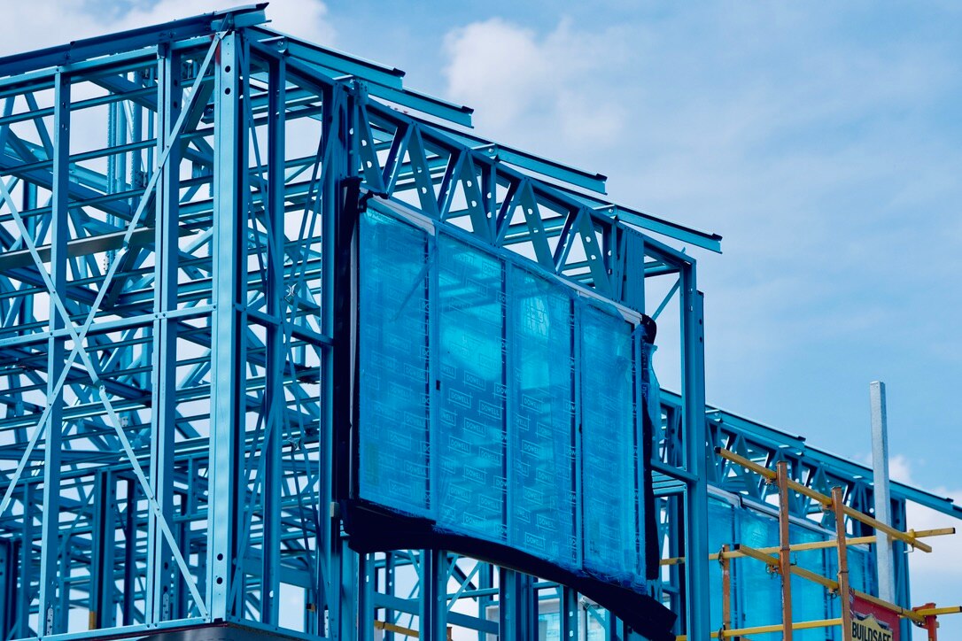 Housing under construction, blue steel frame, large window frame has plastic-covered glass.