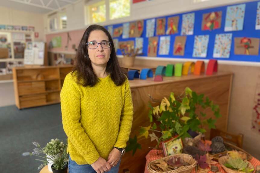 a photo of a woman in mustard jumper looking at the camera, in a kinder playroom 