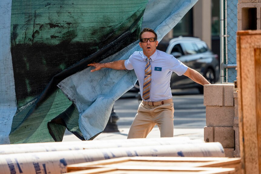 Film still from Free Guy (2021) showing Ryan Reynolds bursting through a canvas sheet and looking alarmed.