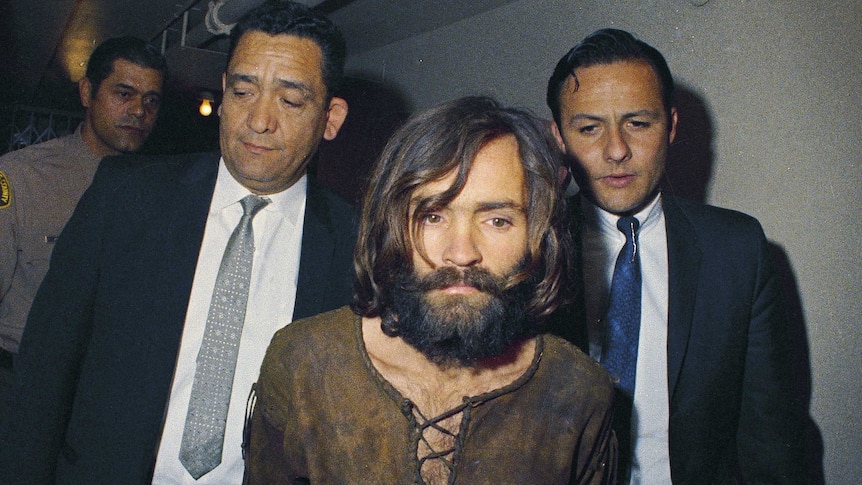 Charles Manson in 1969 is escorted by two men down a corridor to his arraignment on conspiracy-murder charges.