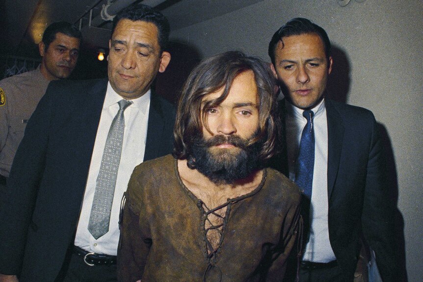 Charles Manson in 1969 is escorted by two men down a corridor to his arraignment on conspiracy-murder charges.