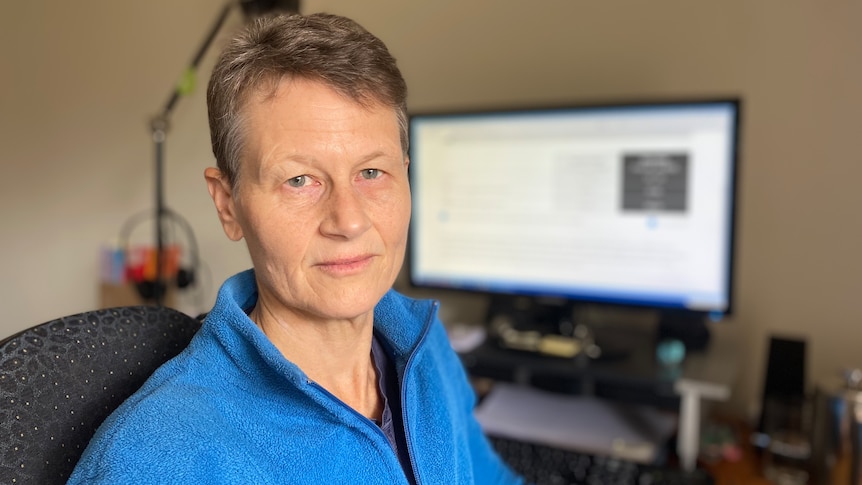 A woman with short hair, blue eyes and a blue jumper looks directly at the camera