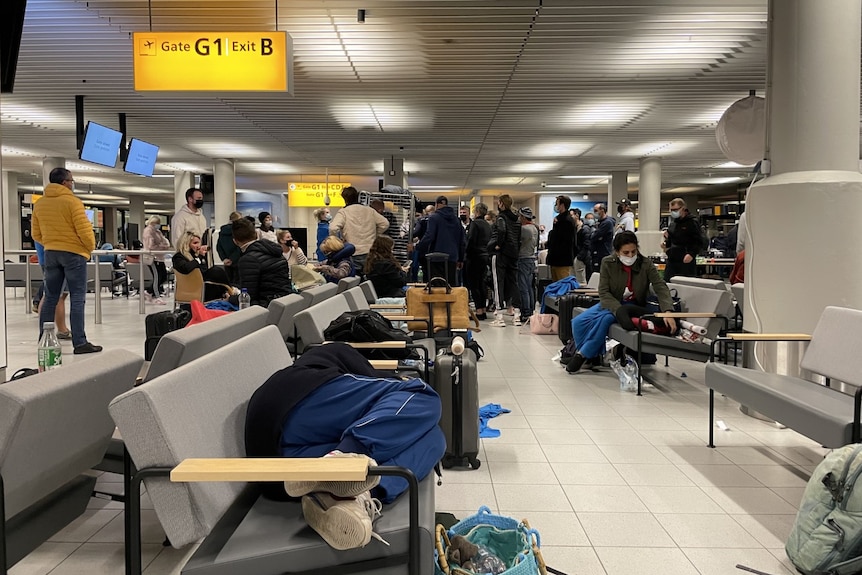 Passengers lay down on chairs and stand around in groups inside an airport terminal