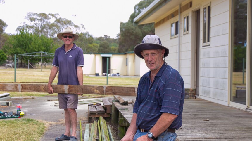 Two men dismantle the verandah of a house