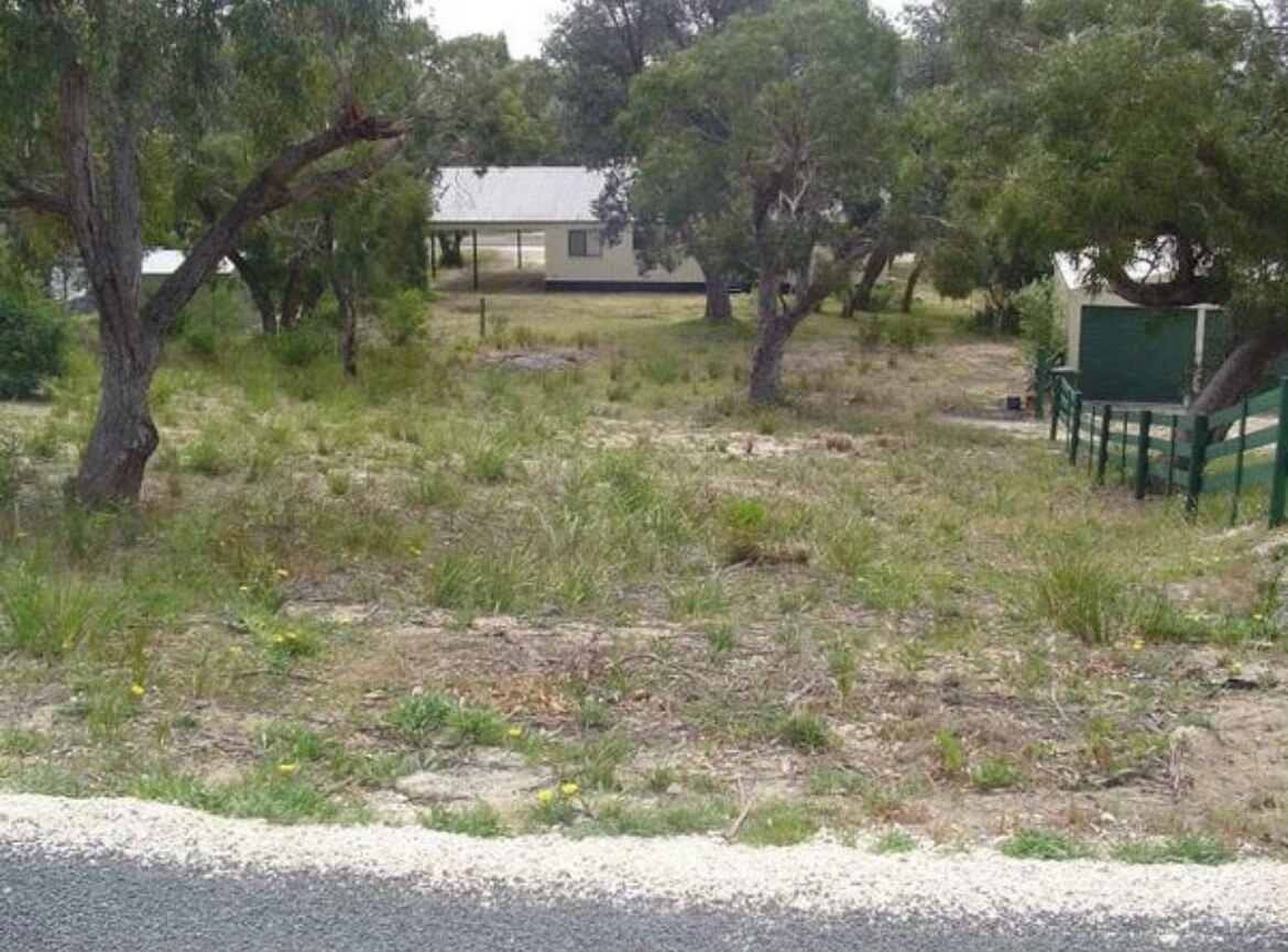 A bushy property lot with a white cottage in the background.
