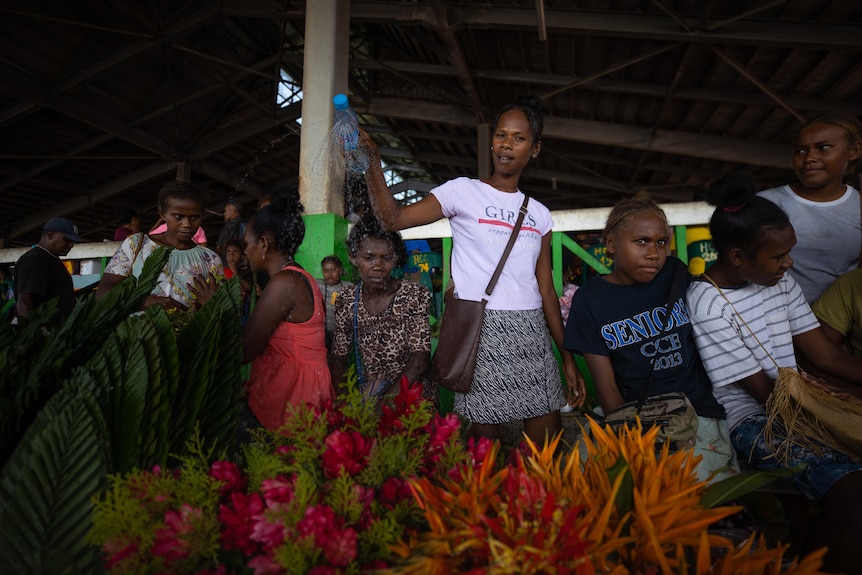 A group of young people stand behind a flower stall in a market. 