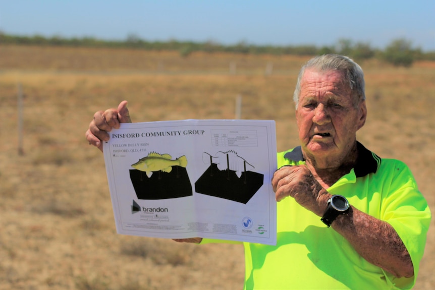 A man in high-vis holds a document showing an image of the yellow fish statue.