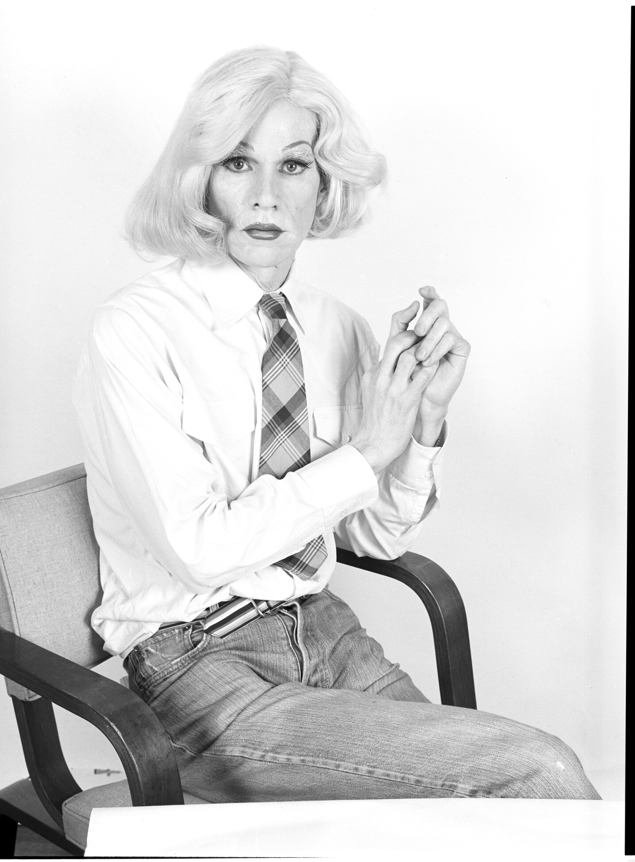 A black-and-white photograph of Andy Warhol wearing a woman's wig and make-up but men's clothes