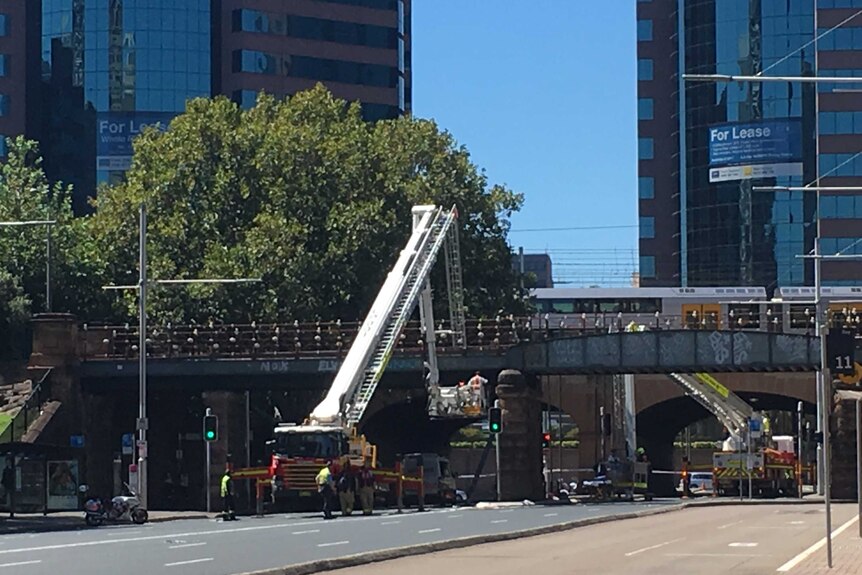 A cherry picker on a fire truck reaches up to the light rail bridge from Central Railway Station.
