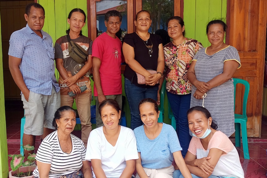 A group of East Timorese people stand together on a front porch, smiling 