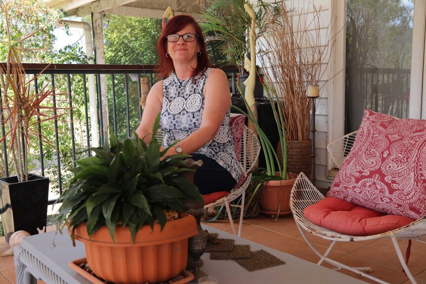 A woman sits on a chair next to some plants