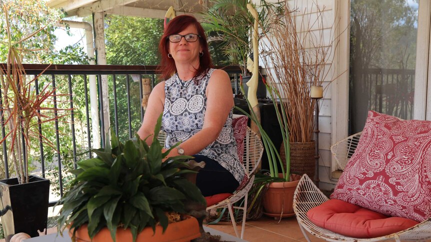 A woman sits on a chair next to some plants