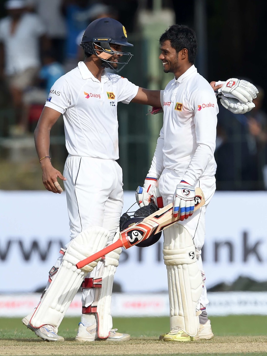 Sri Lanka cricketer Dhananjaya de Silva (R) is congratulated by teammate Dinesh Chandimal on the field.