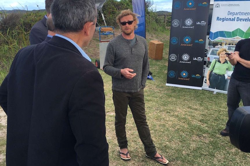A picture of Simon Baker standing on grass talking to WA ministers and ScreenWest officials during a media event.
