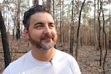 A man looks into the distance with burnt property in the background