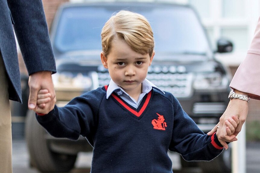 Prince George holds his parents hands and looks coy on his first day of school.