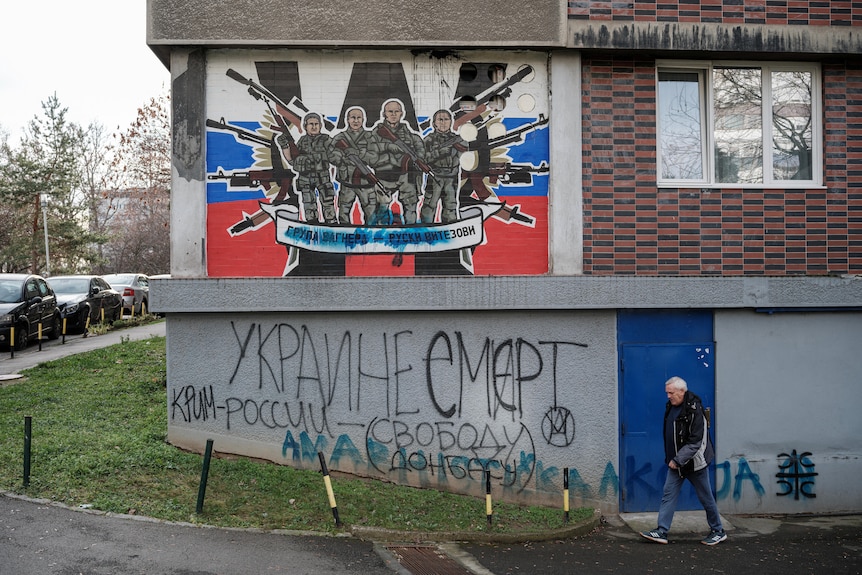 A mural showing soldiers holding machine guns behind the Russian flag and a W is painted on a graffiti wall. 