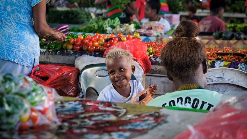 A baby smiles at a passer-by at Honiara's Central Market.