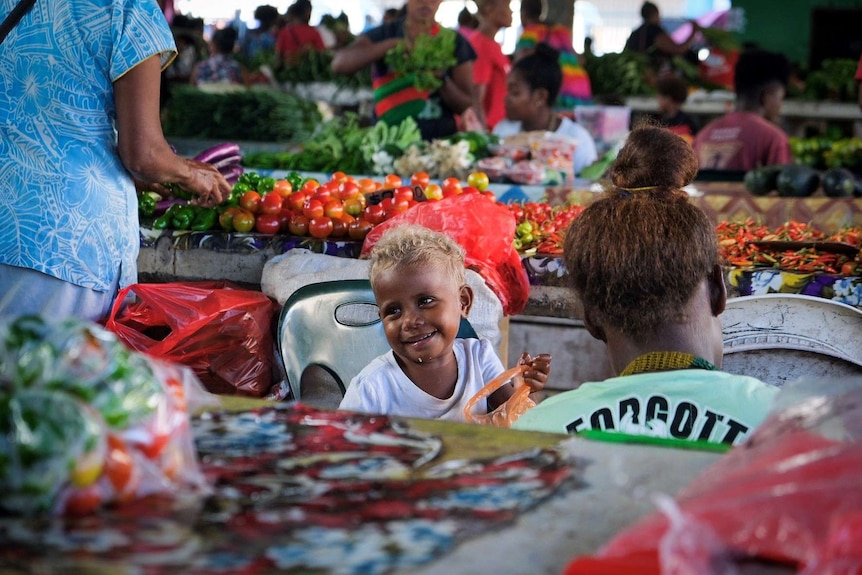 A baby smiles at a passer-by at Honiara's Central Market.