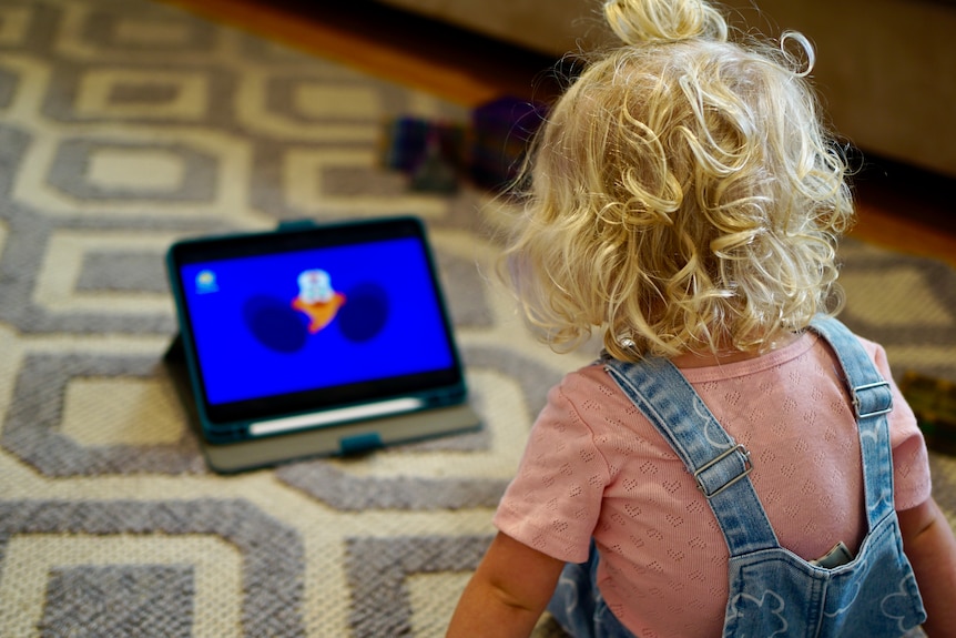 18-month-old Elizabeth is sitting on the floor, watching cartoons on a tablet.
