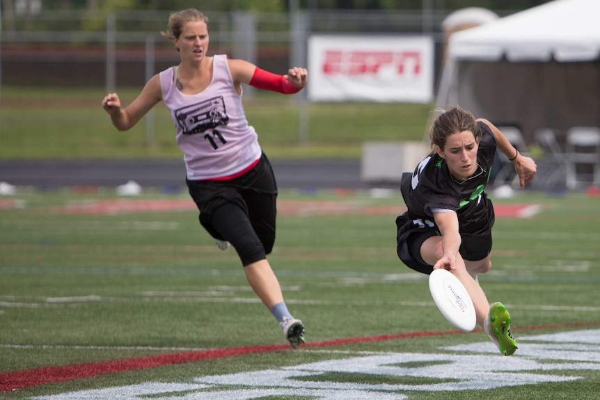 A woman dressed in a sports uniform dives for a frisbee