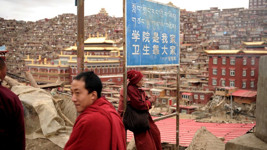 A Buddhist nun sits under a sign at Seda Monastery.