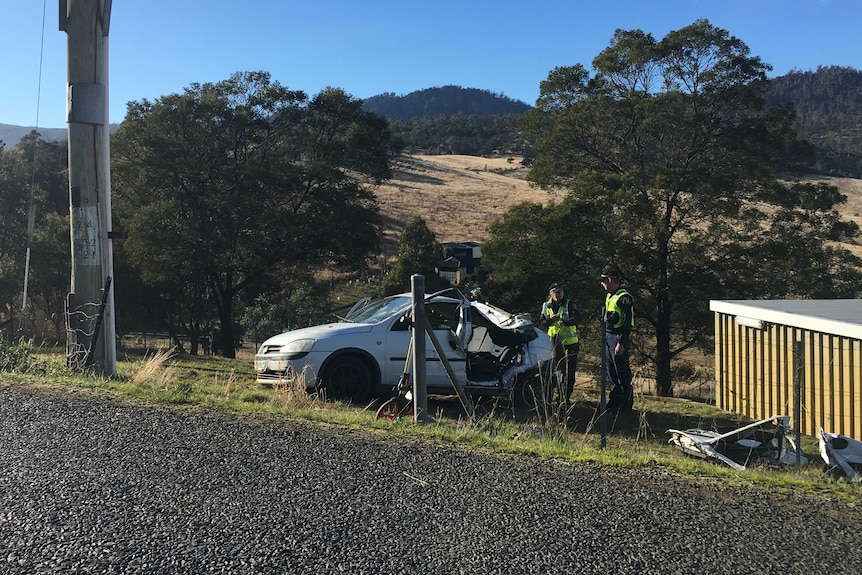 Police officers stand near a car which crashed at Old beach, Hobart.