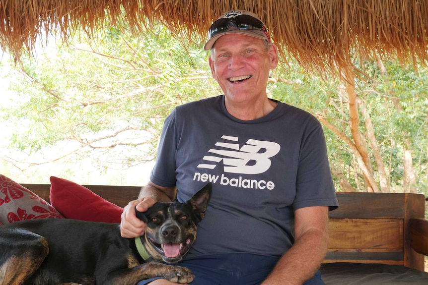 Man smiling at camera with dog resting on lap.