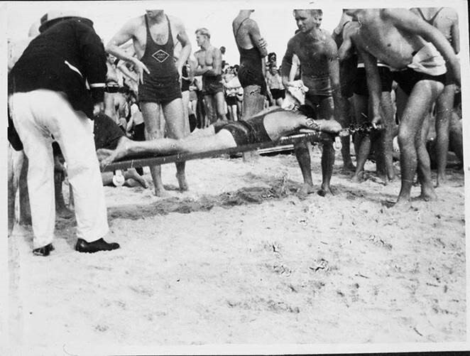 A black and white image of surf lifesavers carrying a man on a stretcher.