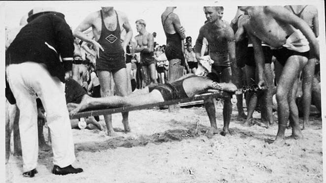 A black and white image of surf lifesavers carrying a man on a stretcher.