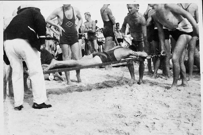 A black and white image of surf lifesavers carrying a man on a stretcher.