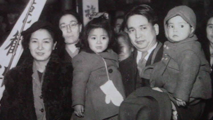 A black and white photo of a Japanese man holding two young children amid a group of people.