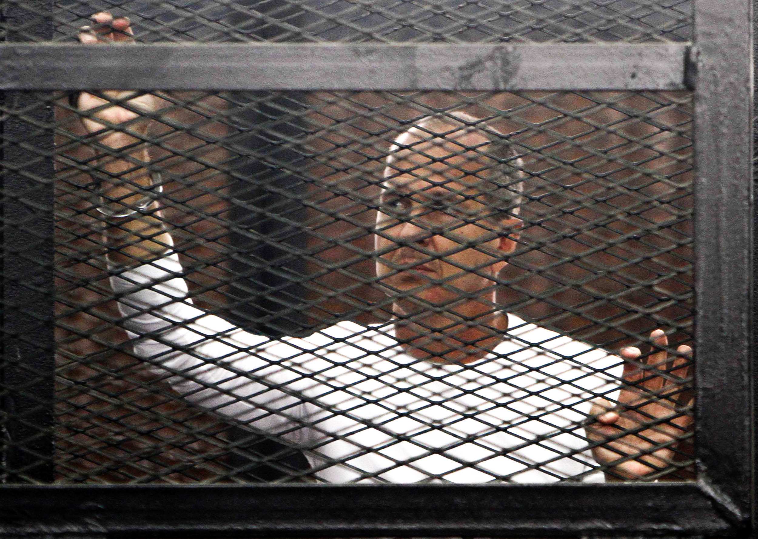 Man behind security screen with hand on screen, looking out with a worried expression on his face.