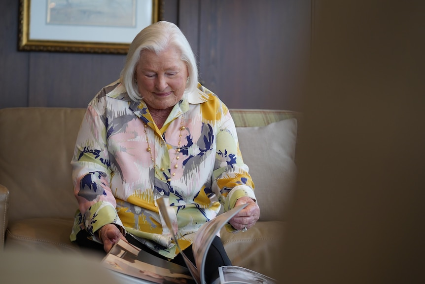 A woman with white hair looks down at a scrapbook