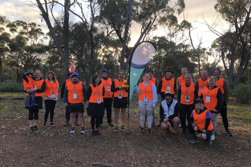 A group of people in orange parkrun vests on a bushy trail.