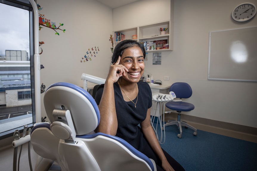 A woman looks over the top of a dental chair and smiles.