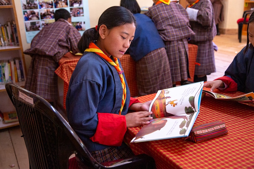 A girl in Bhutan sits in a school looking at a picture book.