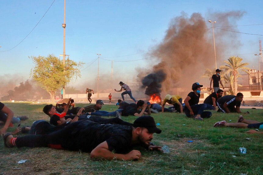A group of protesters take cover, flat on the ground on a lawn in Baghdad as security forces open fire