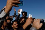 A group of men holding their phone up high take selfies with a Taliban.
