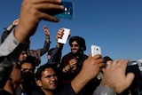A group of men holding their phone up high take selfies with a Taliban.