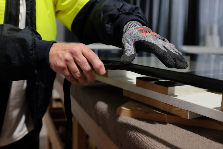 Hands carefully run a piece of rubber film around the edge of a pane of glass.