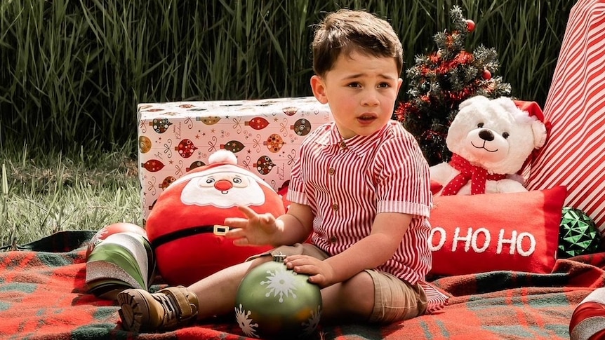 A child sits on a picnic blanket with Christmas decorations around him.