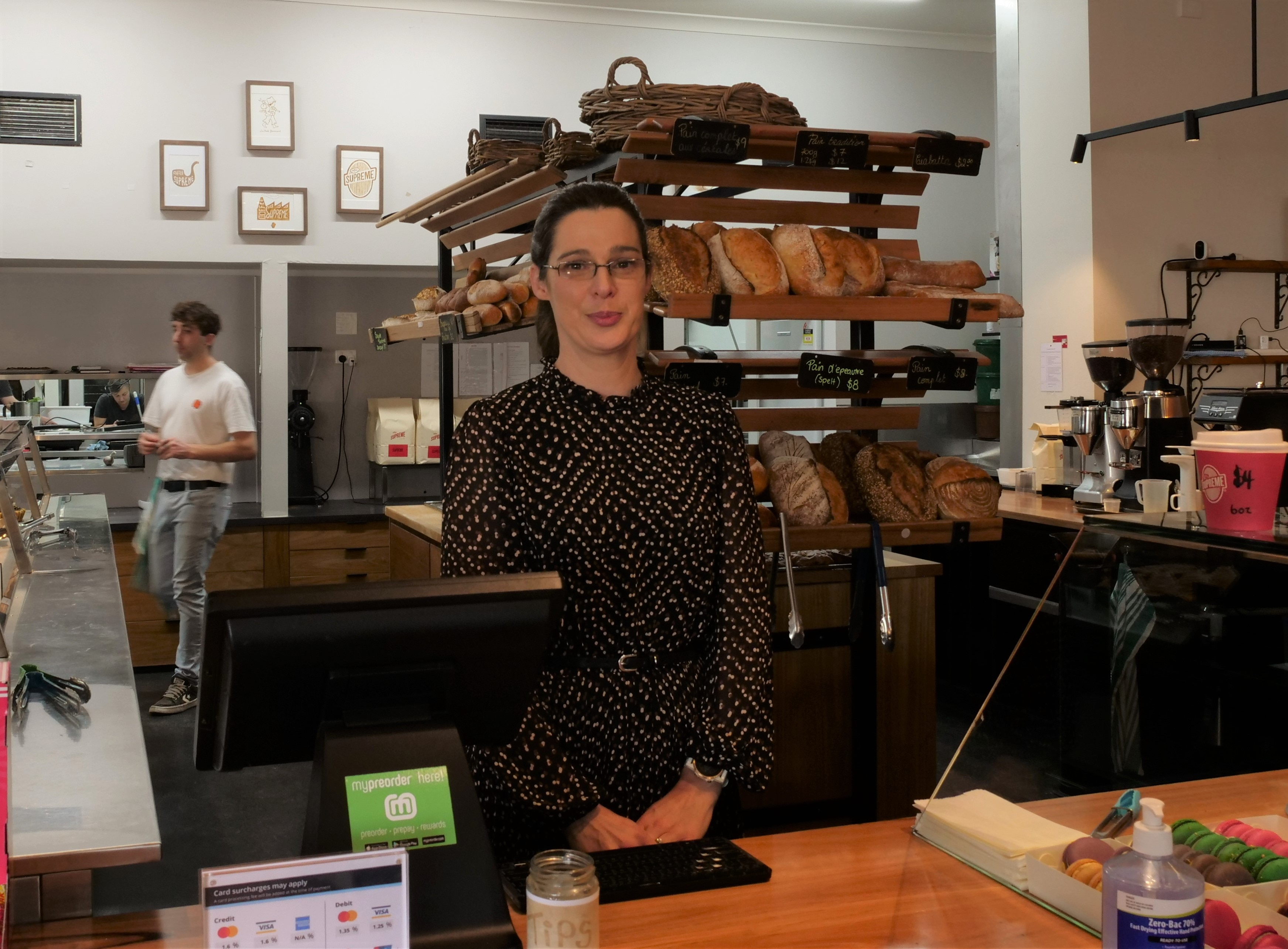 woman in brown dress with slight smile stands in bakery 