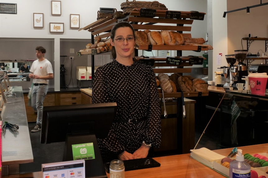 woman in brown dress with slight smile stands in bakery 
