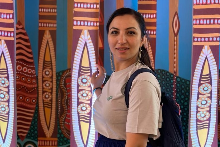 A woman looks at the camera smiling against a backdrop of material.