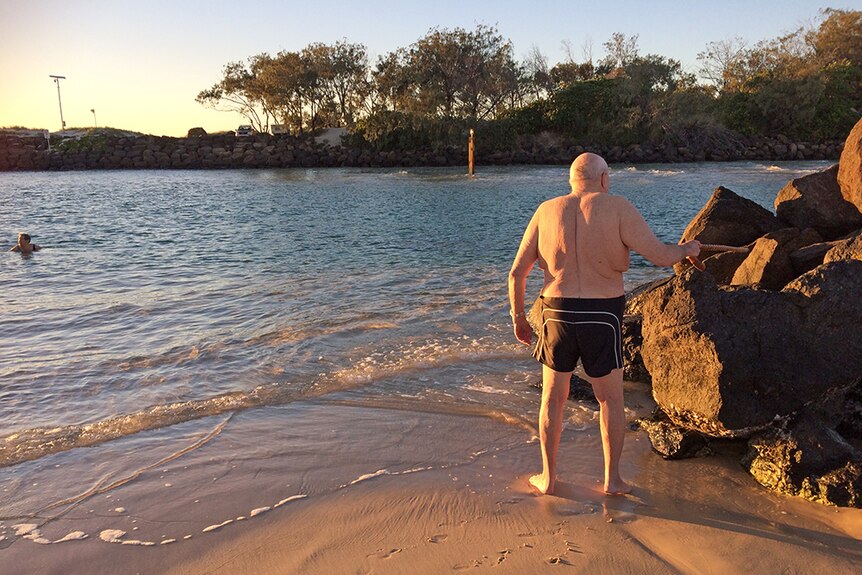 An elderly man puts his walking stick on a rock before taking a swim in the ocean