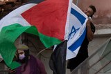 A man kisses the Israeli flag as protesters wave the Palestinian flag