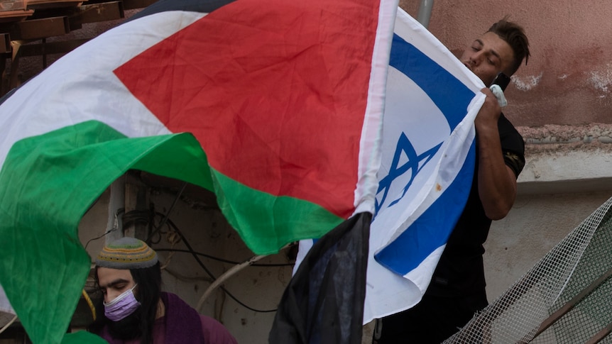 A man kisses the Israeli flag as protesters wave the Palestinian flag