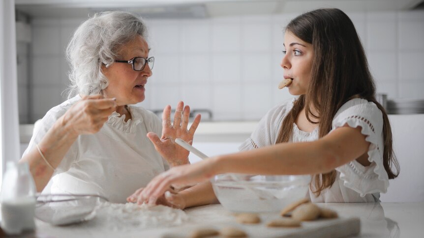 An older woman and a younger woman are sitting in a kitchen baking cookies.
