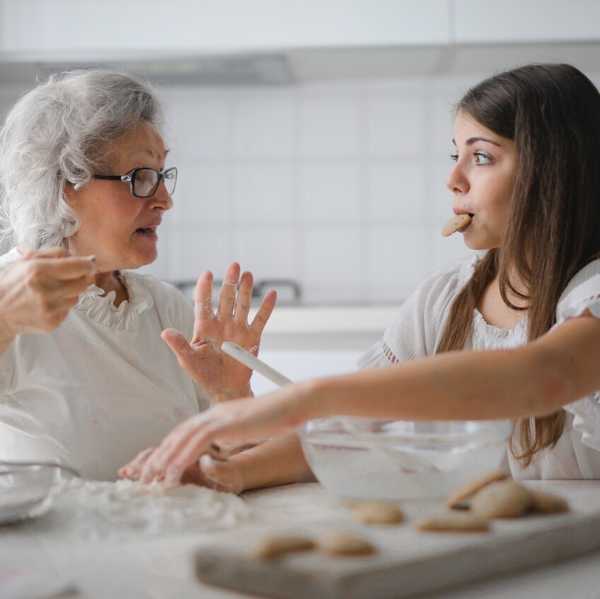 An older woman and a younger woman are sitting in a kitchen baking cookies.